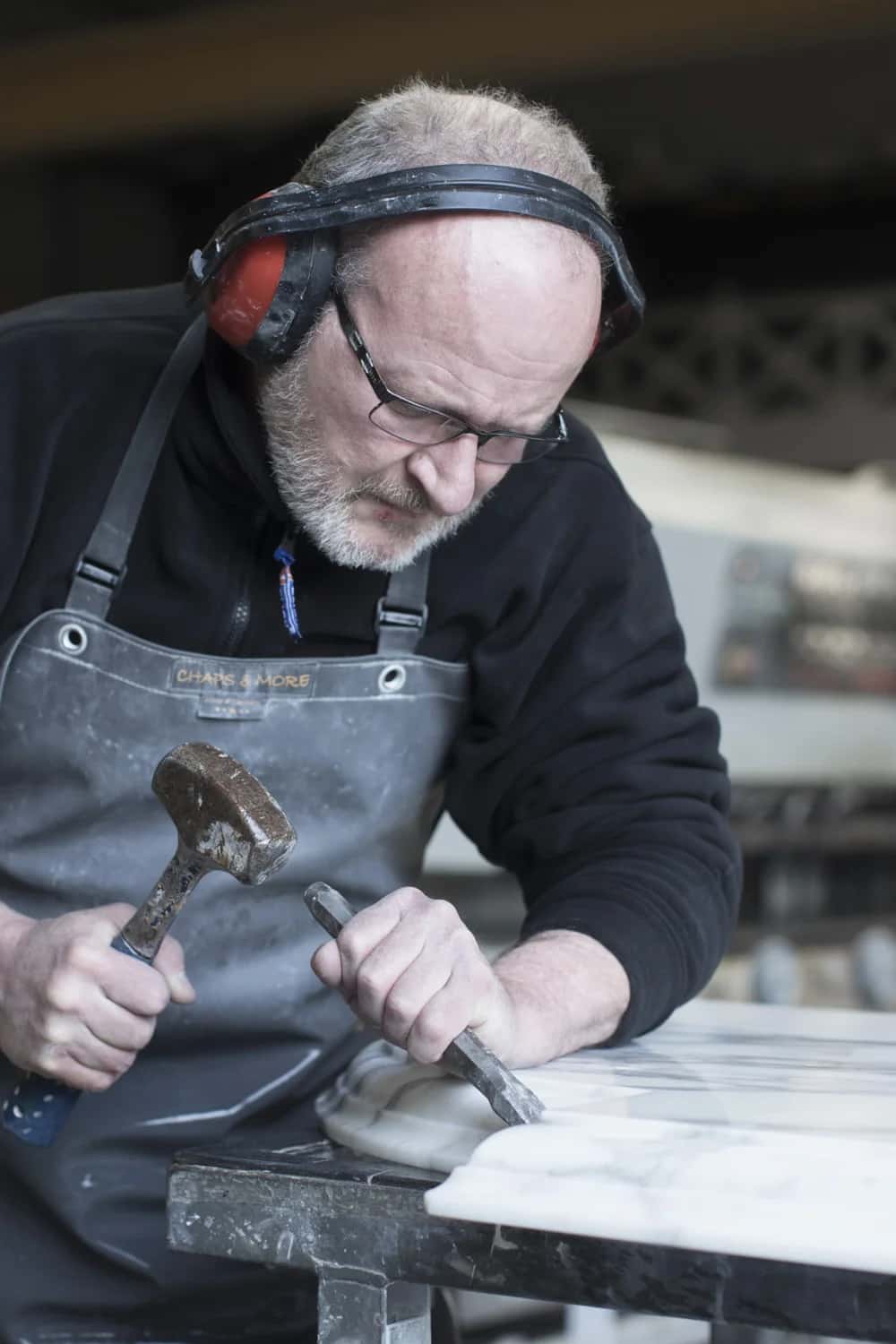 A Miller Brothers craftsman hand-working a stone edge with hammer and chisel